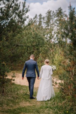 Bir çift yeni evli çift, doğanın yeşilliği tarafından kucaklanan, sakin bir atmosferde sevgi ve birliği sembolize eden manzaralı bir orman patikasında birlikte dolaşırlar.