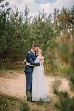 Resmi nikah kılığındaki romantik çift, açık havada sakin bir ortamda kucaklaşıyorlar, yeşillik içinde, doğal ortamda sevgi ve samimiyet sergiliyorlar.