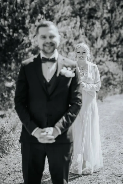 Resmi damat ellerini sıkarak ayakta duruyor, zarif beyaz elbiseli gelin arkadan yaklaşıyor, aşkla dolu güzel bir açık hava düğün sahnesi yaratıyor.