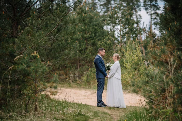 Huzurlu bir ormanda, sevgi ve bağlılığın özünü yakalayan canlı yeşilliklerle çevrili resmi giyinmiş bir çift.