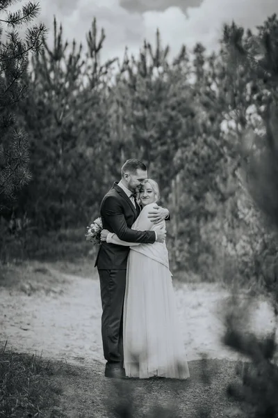 Romantik çift, ağaçlar ve yeşilliklerle çevrili sakin bir ortamda şefkatli bir kucaklaşmayı paylaşıyor, sevgi ve yakınlık hissi uyandırıyor.