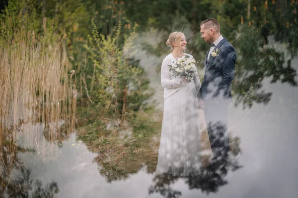 Yeşilliklerle çevrili, güzel bir doğal ortamda duran, özel günlerinde sevgi ve mutluluk gösteren, düğün kıyafetli bir çift.