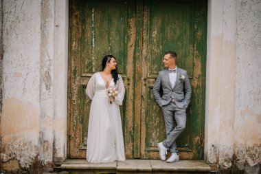 Düğün kıyafetleri içinde bir çift kırsal yeşil kapıların yanında duruyor, mutluluk ve sevgi saçıyor, güzel bir düğün gününün özünü yakalıyorlar.