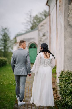 Gelin ve damat, bereketli yeşilliklerle çevrili bir kaldırım taşından yolda birlikte yürürler. Güzel bir açık havada sevgi ve bağlantı gösterirler.