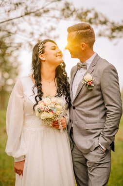 Düğün kıyafetli çift, doğa ile çevrili, güzel ve huzurlu bir atmosferde sevgi ve bağlantı gösteren, neşeli bir anı paylaşıyorlar.