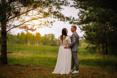 Romantik çift, ağaçlar ve yeşilliklerle çevrili, doğadaki sevgi ve birlikteliğin özünü yakalayan güzel bir doğa sahnesinde kucaklaşır.