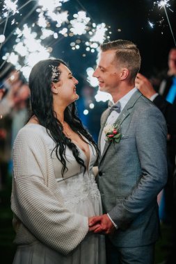 Yeni evli çift birbirine bakıyor, parlak ışıklarla aydınlanıyor, romantik bir ortam yaratıyor, büyülü bir düğün gecesinde aşklarını kutluyorlar.