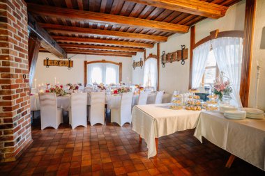 Kutlama için hazırlanmış yemek masaları beyaz masa örtüleri ve çiçeklerle süslenmiş büyük pencerelerden yansıtılan doğal ışıkla aydınlatılmış masalar.