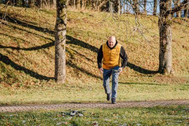 Sarı yelek giyen erkek drone pilotu çimenli bir parkta düşen bir drona doğru koşuyor, aciliyet gösteriyor ve doğal bir ortama odaklanıyor.