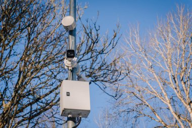 Kontrol kutulu güvenlik kamerası, yapraksız ağaçlar ve açık mavi gökyüzü ile çevrili, açık havada ileri gözetleme teknolojisi sergiliyor.