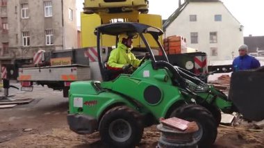Cesis, Letonya - 14 Kasım 2025: Parlak donanımlı operatör inşaat sahasında yeşil sıkıştırıcı kullanıyor, kamera tavaları ve hareket alanına yakınlaştırıyor