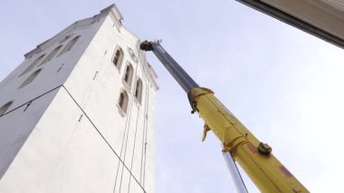 Cesis, Letonya - 14 Kasım 2025: Kamera vinç hareketini yukarı doğru takip ediyor, tarihi beyaz kulenin karmaşık detaylarını gözler önüne seriyor, işçiliği ve yüksekliği vurguluyor