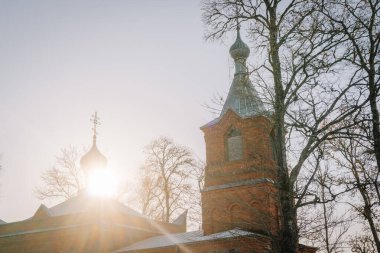 Tuğla kilisede, çıplak ağaçlarla çevrili kubbeli kuleler ve kuleler var. Sıcak güneş ışığıyla yıkanmış. Huzurlu bir ortamda huzurlu bir ortam yaratıyor.