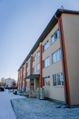 Mazsalaca, Letonya - 15 Kasım 2025: Çağdaş apartman yapısı turuncu sütunlar, büyük pencereler ve karlı bir atmosfer yaratıyor