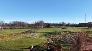 Valmiera, Letonya - 18 Kasım 2025: Güzelim golf sahası manzarası, gür yeşil arazide kayan tepeler ve huş ağaçları ve kamera kapları sorunsuzca hareket ediyor.