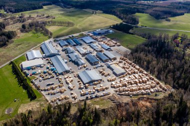 Valmiera, Letonya - 01 Mayıs 2021: Yukarıdan ele geçirilen büyük kereste deposu, bereketli yeşilliklerle çevrili odun yığınları ve depolama binaları