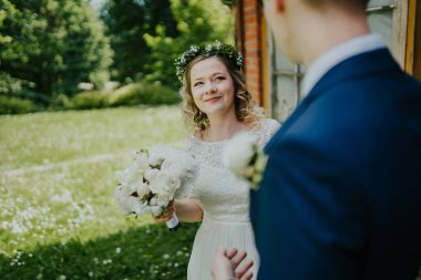 Gelin, damada güzel bir açık havada gülümsüyor, canlı yeşilliklerle çevrili, romantik ve neşeli bir atmosfer yaratıyor.