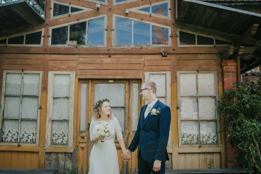 Çiftler kırsal bir ahşap yapının önünde el ele tutuşup gülümsüyorlar. Açık hava düğününde sevgi ve neşeyi somutlaştırıyorlar.