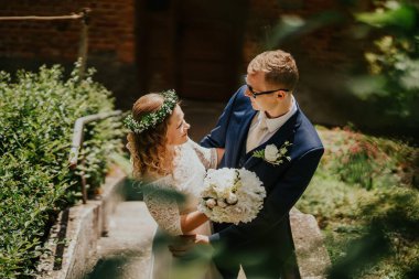 Güzel bir bahçede, birbirine bir buketle sarılan, canlı yeşilliklerle çevrili, huzurlu bir atmosferde sevgi ve mutluluk saçan bir çift.