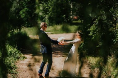 Zarif kıyafetler içindeki erkek ve kadın, kırsal bir yolda duruyorlar, yemyeşil bir buketin ortasında bir buketi değiş tokuş ediyorlar, sakin bir ortamda romantizmi ve mutluluğu somutlaştırıyorlar.