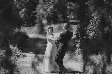 Mutlu çift düğün kıyafetleri içinde ağaçlar ve yeşilliklerle çevrili gür bir ormanda dans ederek doğada bir aşk ve neşe anı yakalıyorlar.