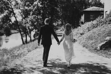 Düğün kıyafetleri içinde bir çift nehir kenarında yürür, doğanın güzelliğiyle kucaklaşır, özel günleri için sakin ve romantik bir atmosfer yaratır.