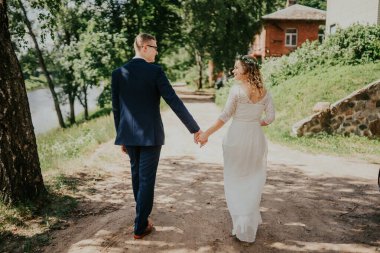 Bir çift yeni evli, doğa tarafından kucaklanan, güzel bir toprak yolda yürüyor. Açık havada sevgi ve neşelerini sergiliyorlar.