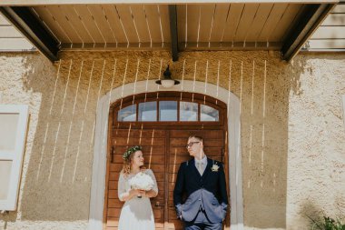 Düğün kıyafetli çift ahşap kapının yanında durur, güneş ışığı güzel gölgeler yaratır, aşkın özünü yakalar ve dışarıda büyüleyici bir şekilde kutlarlar.