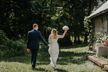 Çiftler güzel bir bahçede birlikte yürürler, yeşil ve güneş ışığıyla çevrili, düğün günlerini mutluluk ve aşkla kutlarlar.