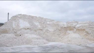 Endüstriyel ayar büyük sentetik alçıtaşı yığınları içerir ve sahne boyunca materyalin dokusunu ve ölçeğini kademeli olarak gösteren bir kamera yakınlaşması vardır.