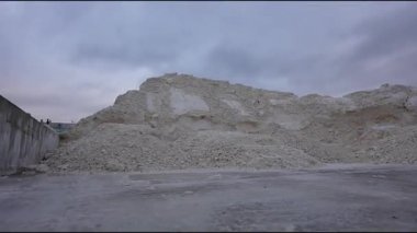 Endüstriyel dekor, sahnedeki dokuları ve mekansal ilişkileri vurgulayan kademeli bir kamera zoom ile büyük sentetik alçıtaşı yığınları içerir.