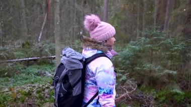 Smiltene, Letonya - 23 Kasım 2025: Canlı kış kıyafetleri içindeki kadın yürüyüşçü dingin ormanda yürürken, kamera onu takip ediyor.