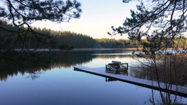 Bereketli yeşilliğin ortasında ahşap bir rıhtıma sahip huzurlu göl manzarası, sakin su yansımalarını ve doğal güzellikleri yakalamak, sakin atmosferi geliştirmek için kamera tavaları.