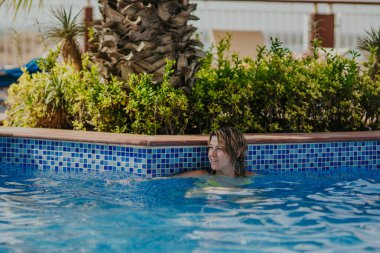 Havuzda ferahlatıcı bir yüzüşten hoşlanan dişi canlı fayanslar ve tropikal bitkilerle sakin bir atmosfer yaratıyor, rahatlama ve rahatlama için mükemmel.