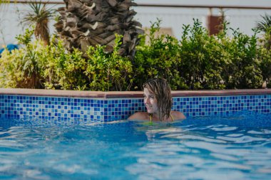 Dişi, yemyeşil ve renkli fayanslarla çevrili bir havuzda ferahlatıcı bir yüzüşün keyfini çıkarıyor, rahatlama ve rahatlama için sakin bir atmosfer yaratıyor.