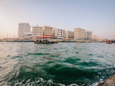 Dubai, Suudi Arabistan - 21 Ekim 2019: Abra gemisi Dubai Deresi 'nde yolcuları canlı şehir silueti ve güneş ışığını yansıtan sakin suyu ile taşır.
