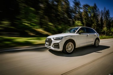 Ogre, Letonya - 11 Mayıs 2024 - Düğün çiçekleriyle süslenmiş beyaz Audi SUV, hareket bulanıklığı ve dinamik ve romantik bir seyahat sahnesi yaratarak güneşli bir yolda hızla ilerliyor..