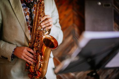 Müzisyen canlı bir mekanda saksafonla performans sergiliyor, enstrümanın parlaklığını sıcak ahşap ve yumuşak aydınlatmaya vurguluyor, davetkar bir atmosfer yaratıyor.