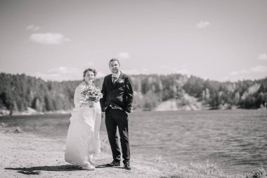 Zarif gelin ve damat, doğa ile çevrili sakin göl kenarında poz verir. Açık havada güzel bir düğün ortamında sevgi ve bağlılık gösterirler.