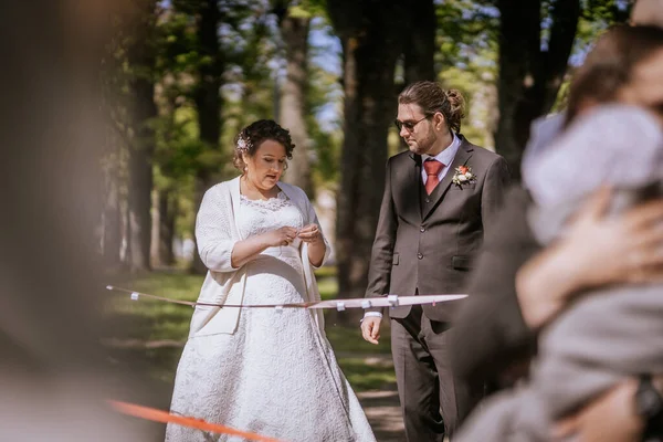 Zarif gelin ve damat, yeşil ve ağaçlarla çevrili güzel bir parkta birlikte yürüyorlar. Aşk dolu romantik bir düğün ortamı sergiliyorlar.