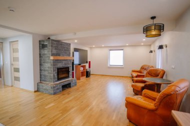 Kahverengi deri koltukları, şık bir şöminesi ve ahşap döşemesi olan, rahat ve havadar bir ortamda sosyal etkileşim için tasarlanmış oturma odası.