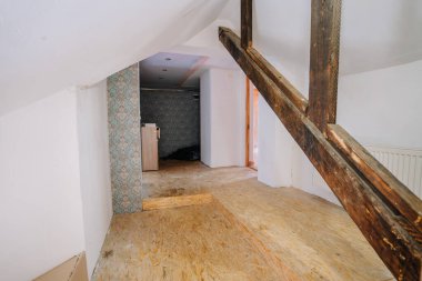 Kısmen yenilenmiş tavan arası, ahşap kirişler ve aydınlık duvarlar, desenli bir aksan duvarı, yaratıcı iç tasarım potansiyelini vurguluyor.