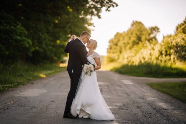 Bir çift, sakin bir kır yolunda samimi bir anı paylaşıyor, yeşilliklerle çevrili, açık havada resim gibi bir düğün sahnesinde aşkı ve birliği kutluyor.