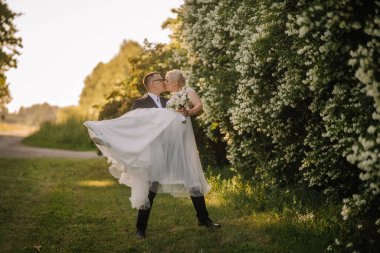 Güzel bir doğa ortamında neşeli bir öpücük paylaşan çift, canlı çiçekler ve yeşillikler özel günleri için romantik bir ortam yaratıyor.