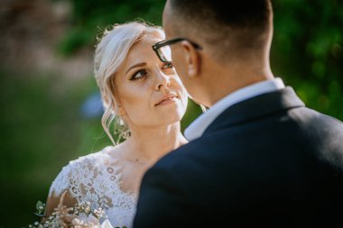 Dantelli gelinlik giymiş gelin, doğa ile çevrili düğün töreninde damada bakar. İki insan arasındaki samimi aşk ve bağın görüntüsünü yakalar.