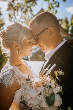 Çiftler romantik bir açık hava ortamında kucaklaşıyorlar, güneş ışığı onların özelliklerini vurguluyor ve yemyeşil sakin bir atmosfer yaratıyor, aşkı ve birliği simgeliyor.