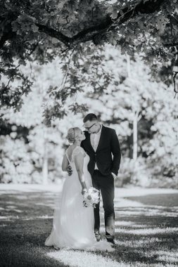 Resmi nikah kılığındaki çift, bir ağacın altında romantik bir anın tadını çıkarıyorlar, canlı bir arka planı var, sevgi, neşe ve bağlılık sergiliyorlar.