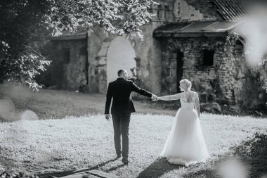 Resmi giyinmiş bir çift, yeşil ve taştan yapılarla birlikte sakin bir ortamda yürüyorlar. Özel günleri için romantik bir ortam yaratıyorlar.