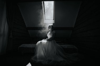 Zarif beyaz elbiseli gelin, yatakta, tavan penceresinden gelen yumuşak ışıkla yıkanmış, sakin bir atmosferle çevrili, romantizm ve sükuneti çağrıştıran duygular içinde.