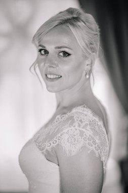 Sarı saçlı, narin dantel bir elbise giymiş güzel gelin, yumuşak bir ışıkta poz veriyor, zarafet ve romantizmin özünü büyüleyici bir gelin anında yakalıyor.